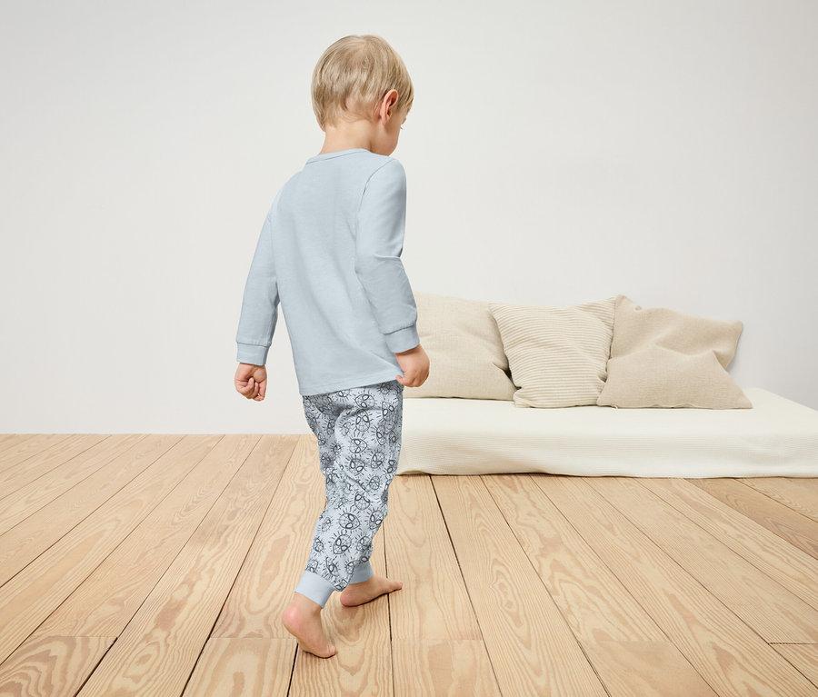 Ein Junge im Schlafanzug geht über einen Holzboden. Im Hintergrund ist ein Bett mit Kissen zu sehen.