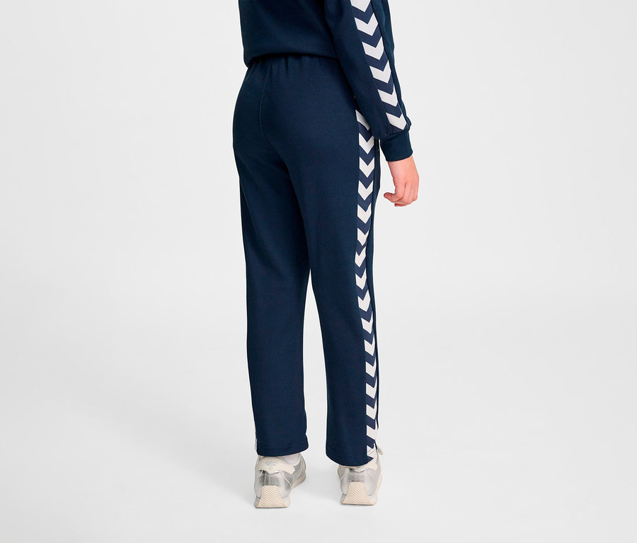 Person von hinten trägt marineblaue HUMMEL HMLJR Archive Regular Poly Pants mit weißen Chevrons an der Seite.