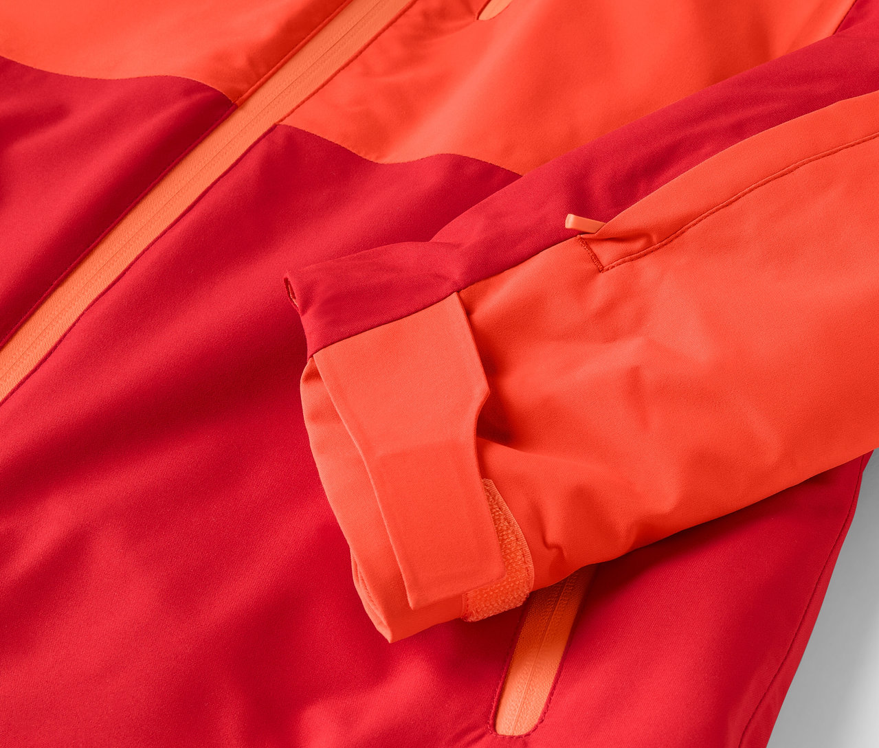 Detailaufnahme einer rot-orangen Jacke, wobei der Ärmel sichtbar ist.