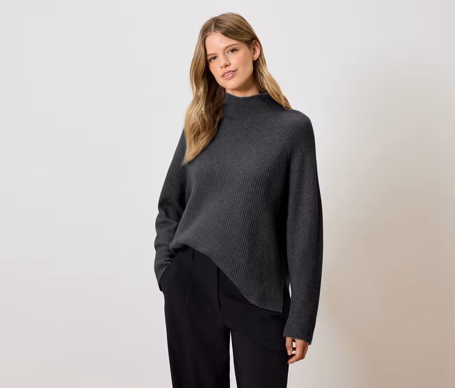 Frau posiert in einem grauen Rollkragenpullover und einer schwarzen Hose.