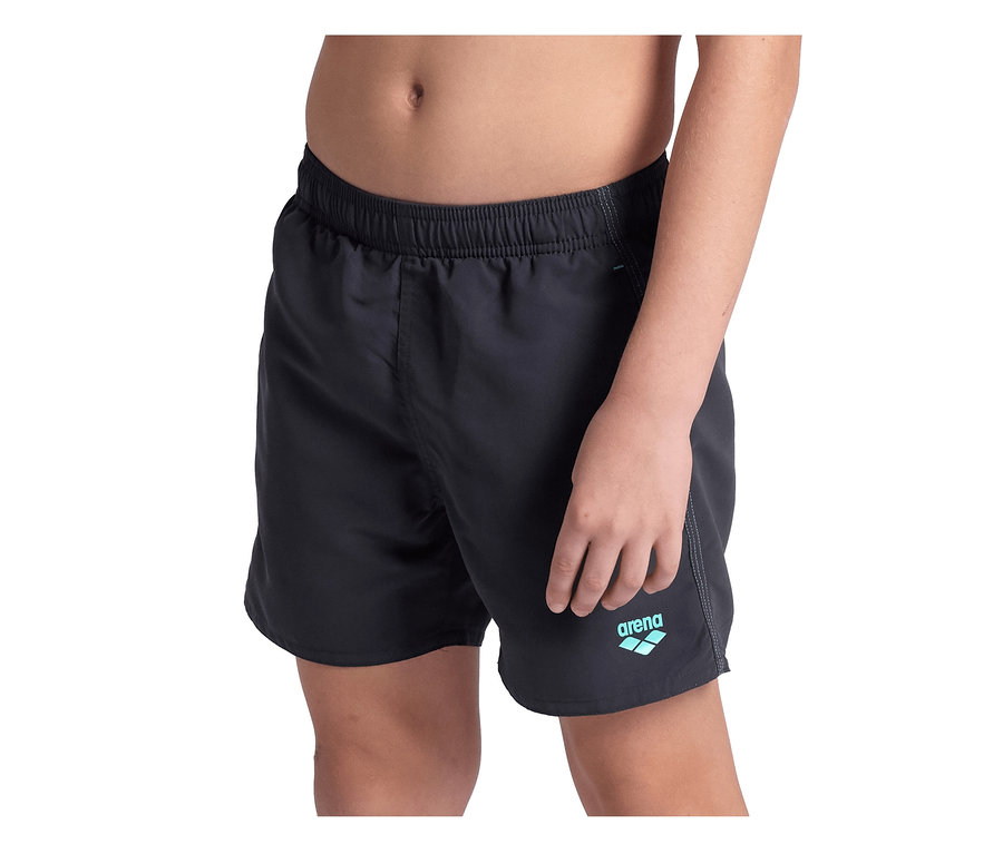 Kind trägt schwarze arena Kinder-Beach Boxer Solid R Badehose mit hellblauem arena Logo am linken Bein.