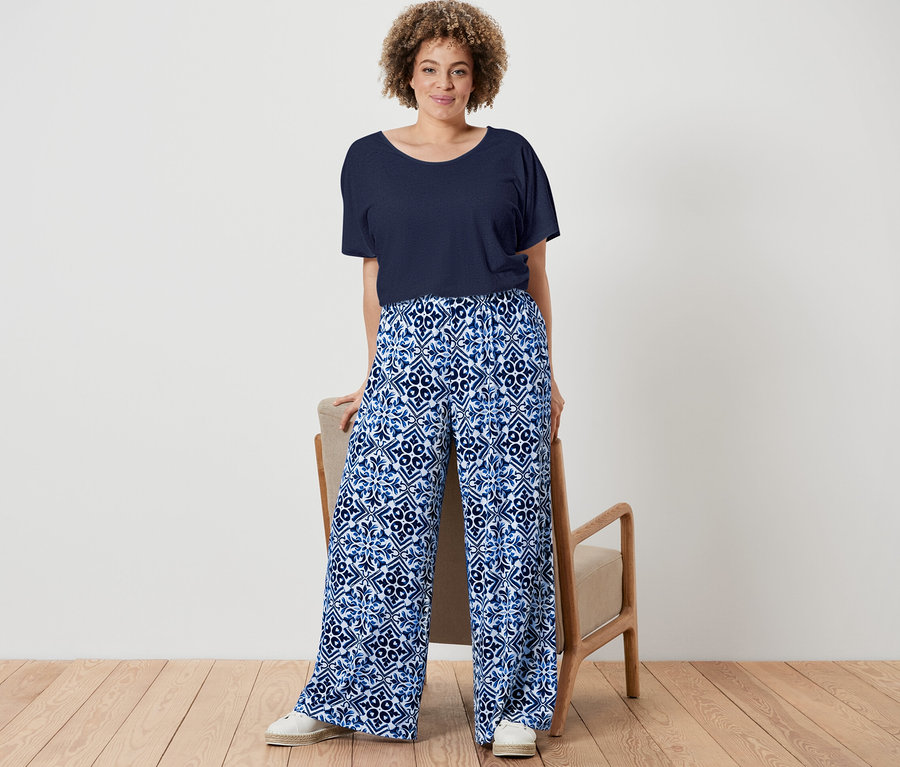 Eine Frau posiert in einem marineblauen Shirt aus Leinenmix und einer blauen, bedruckten Palazzohose.