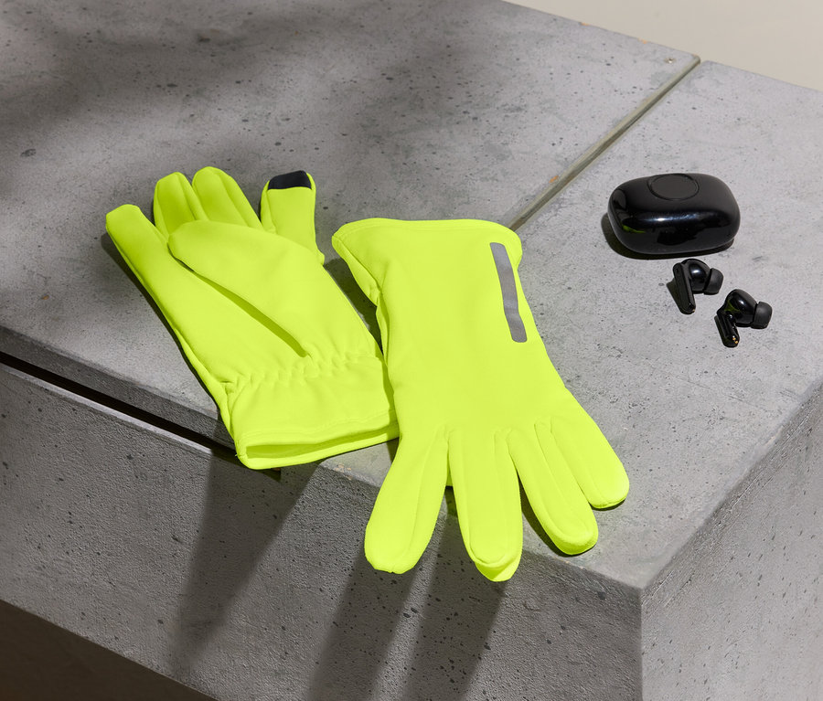Zwei neon-gelbe Handschuhe und schwarze Ohrhörer mit Etui auf einer Betonoberfläche.
