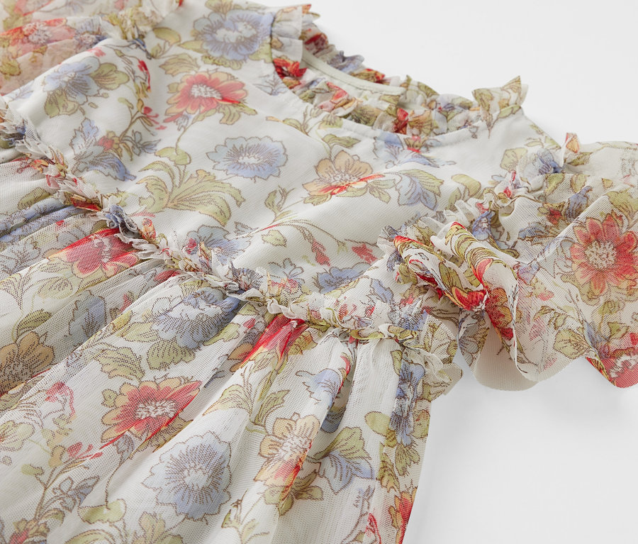 Detailansicht eines Kinder-Tüllkleids mit Blumenmuster und Rüschen.