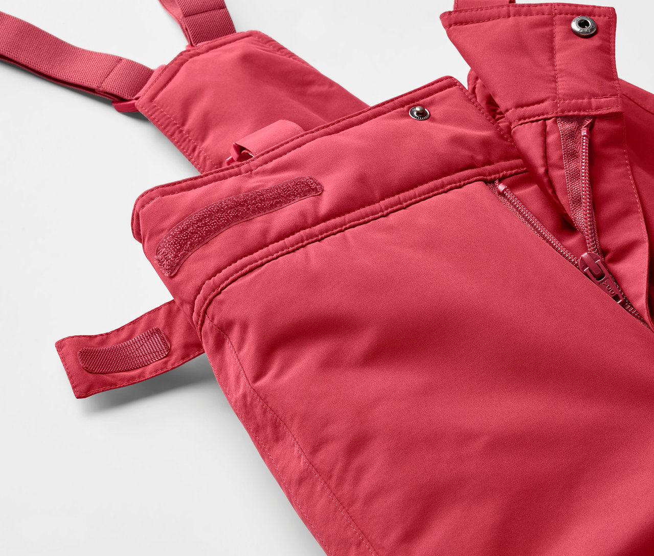 Detailaufnahme einer roten Skihose mit Latz und Reißverschluss.