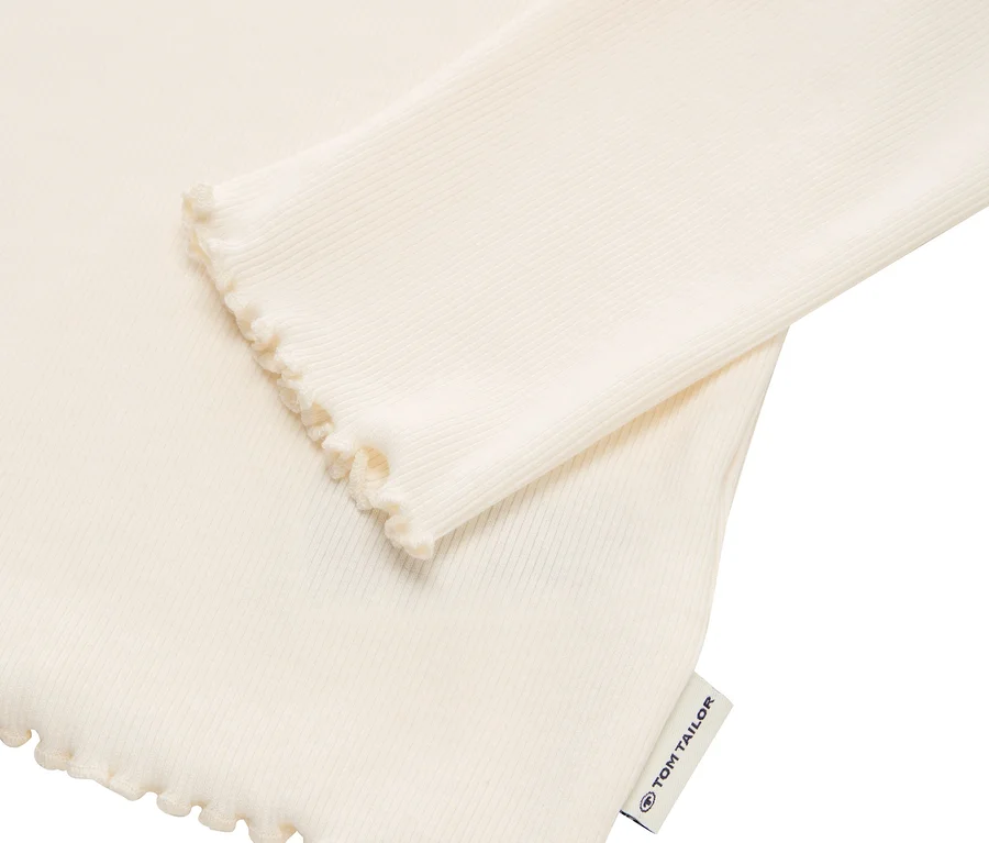 Detail eines cremefarbenen, gerippten Langarmshirts mit Rüschenkante und Tom Tailor Etikett.