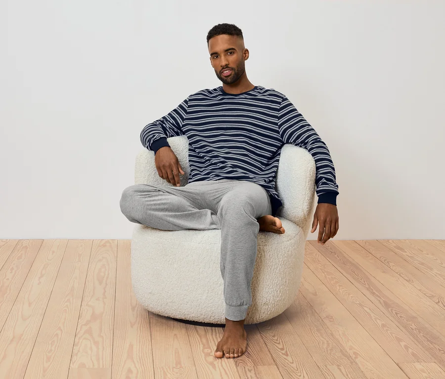 Mann sitzt in einem Sessel. Er trägt ein gestreiftes Langarmshirt und eine graue Jogginghose.