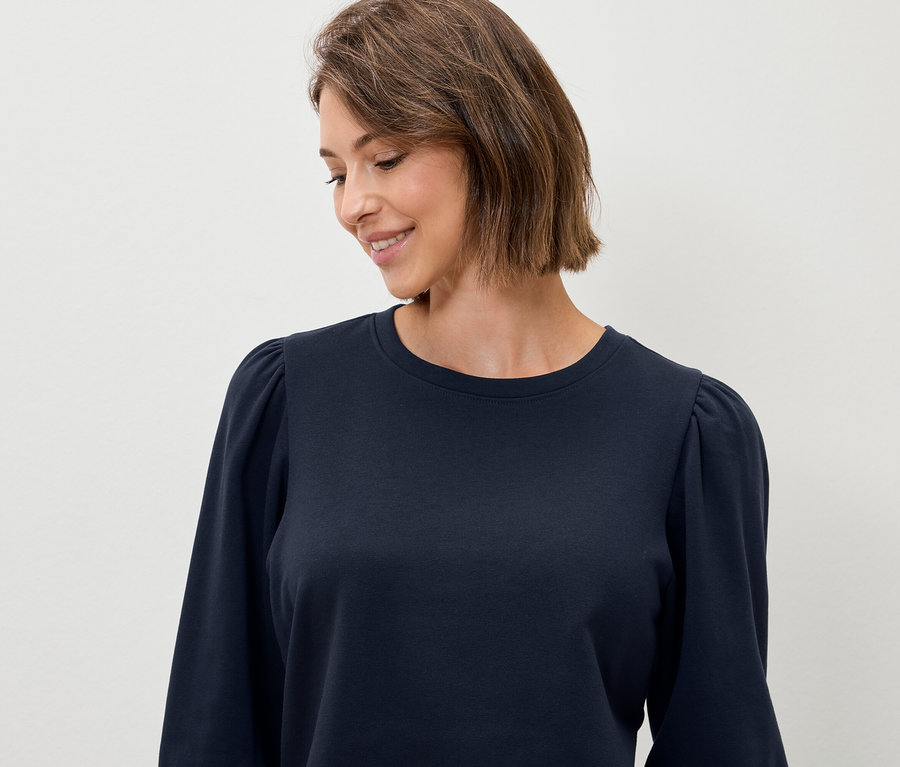 Frau mit kurzem braunem Haar trägt ein dunkelblaues Langarmshirt.