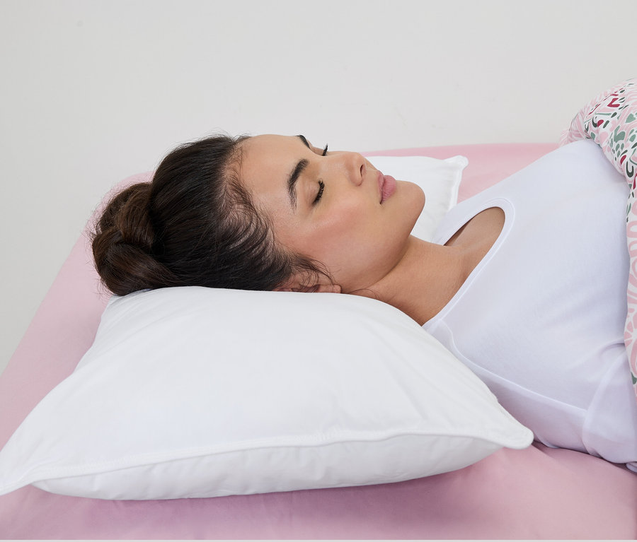 Frau schläft auf einem weißen irisette® Wasserkissen auf einem rosa Bettlaken.