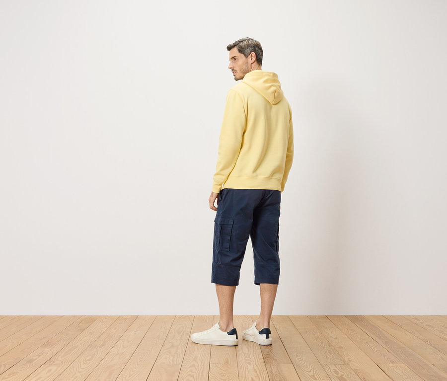 Mann von hinten, mit gelbem Hoodie, blauen Shorts und weißen Turnschuhen.