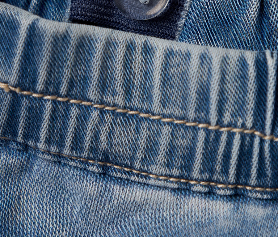 Detailaufnahme von hellblauen Jeans mit einem verstellbaren Gummibund und einem transparenten Knopf.