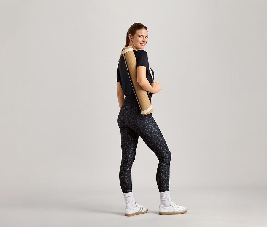 Frau mit Yogamatte über der Schulter, trägt ein schwarzes Sportshirt.