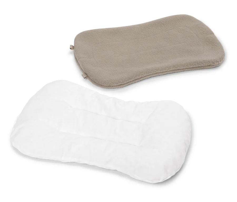 Ein weißes, gestepptes Kissen liegt unter einem beige Kissen auf einem weißen Hintergrund.