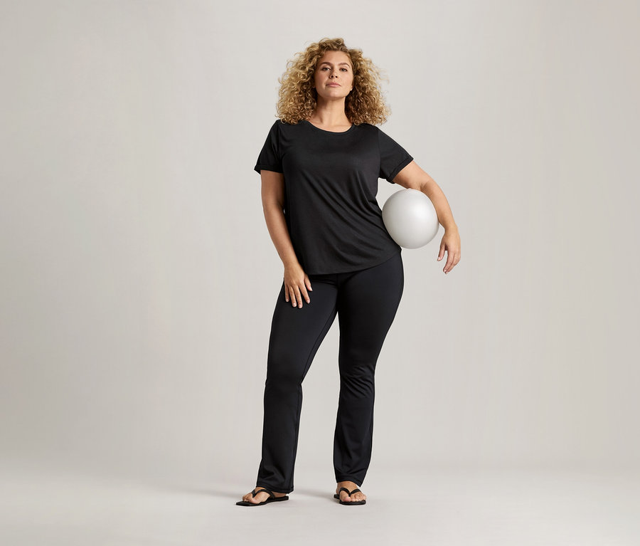 Frau mit lockigem Haar, schwarzem T-Shirt und schwarzen Hosen hält einen weißen Ball.