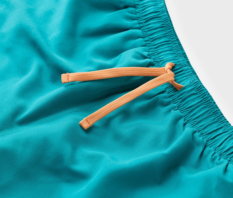 Nahaufnahme einer türkisfarbenen Badeshorts mit orangefarbenem Kordelzug.