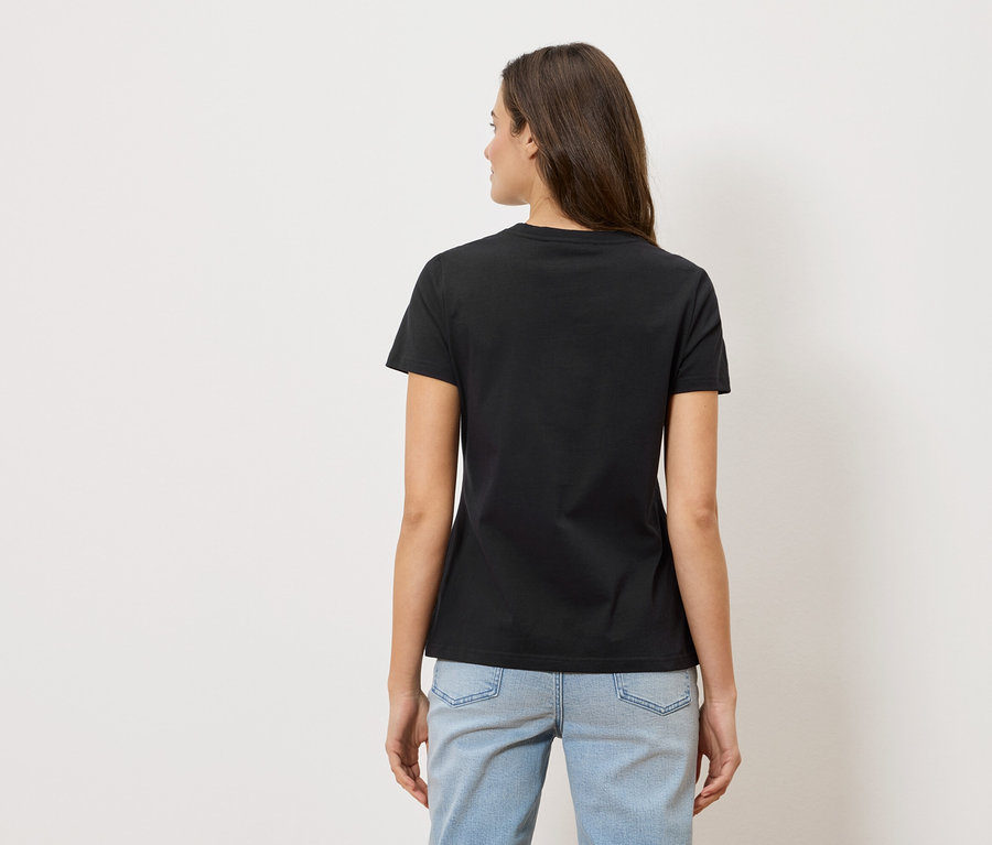 Rückansicht einer Frau mit langen braunen Haaren, die ein schwarzes T-Shirt und hellblaue Jeans trägt.