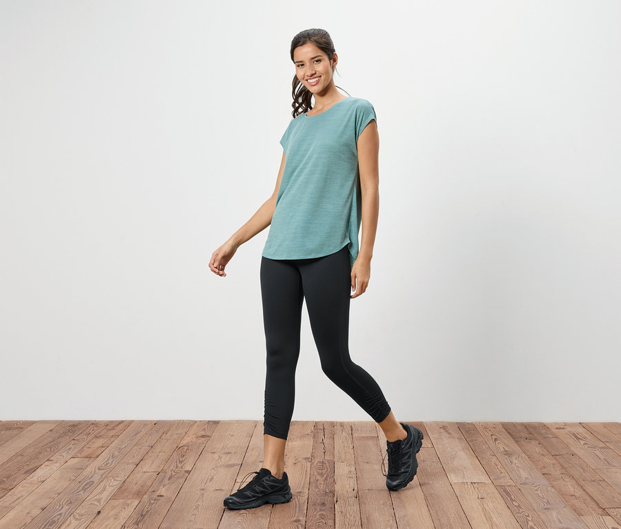 Frau geht in einem türkisfarbenen T-Shirt, schwarzen Leggings und schwarzen Turnschuhen.