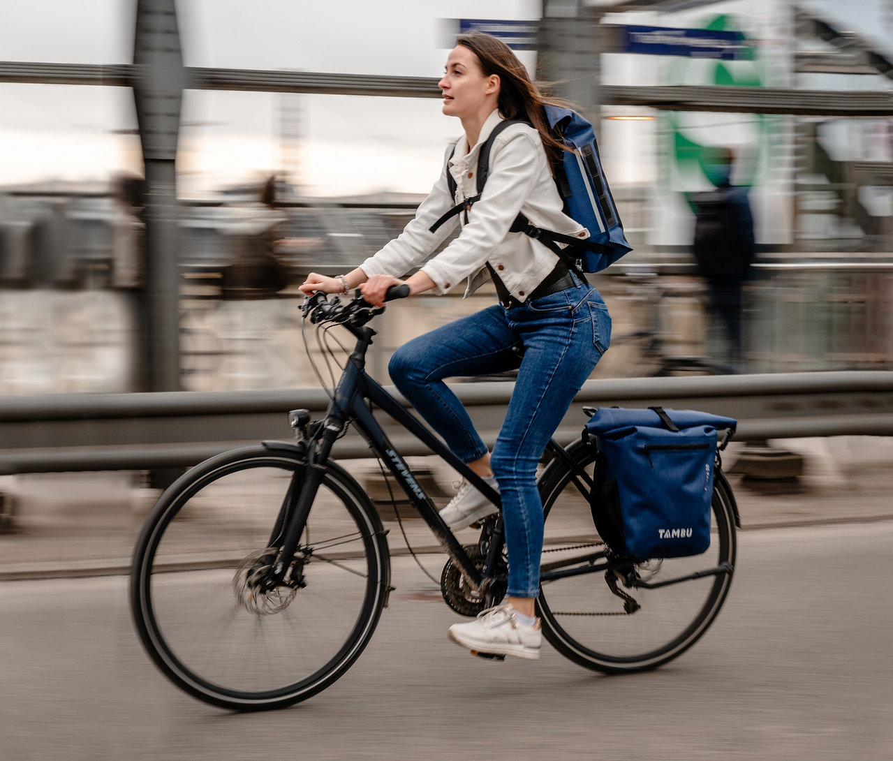 Frau fährt mit Fahrrad mit blauen Tambu »INAYA« Fahrradtaschen auf Gepäckträger und Rücken.