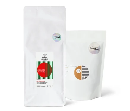 Zwei weiße Kaffeepackungen nebeneinander. Eine Packung ist Espresso Probierpaket "Co-Roast Duo".