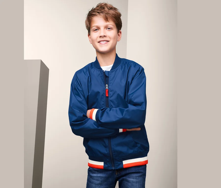 Ein lächelnder Junge posiert in einer blauen Bomberjacke mit recyceltem Material.