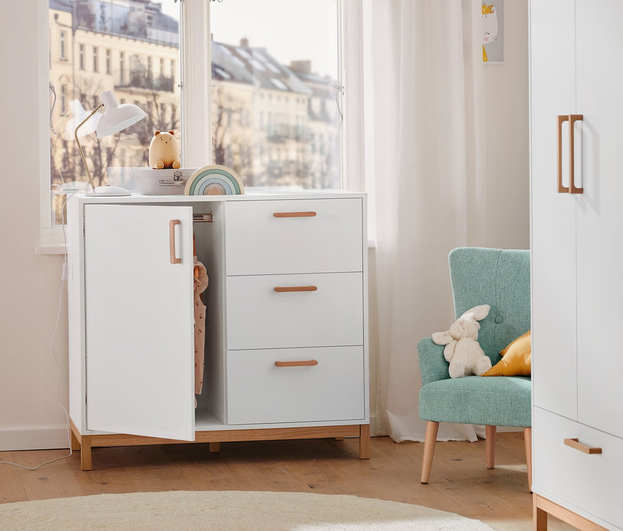 Helles Kinderzimmer mit weißer 2-in-1: Kommode und Kleiderschrank, türkisfarbenem Sessel und Stofftier.