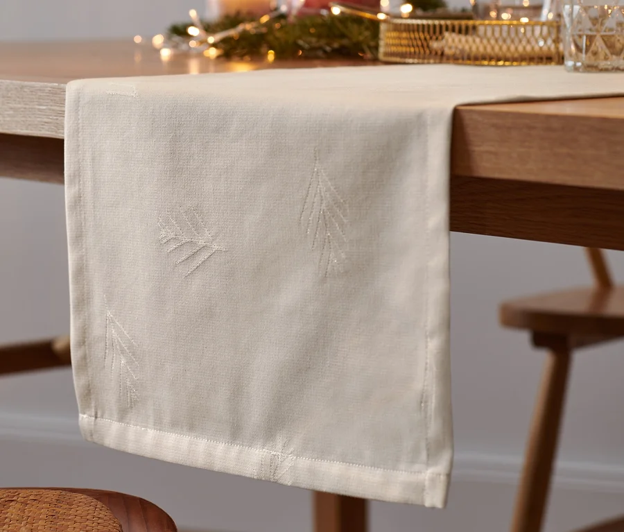 Ein offwhite Jacquard-Tischläufer liegt auf einem Tisch mit Weihnachtsschmuck.