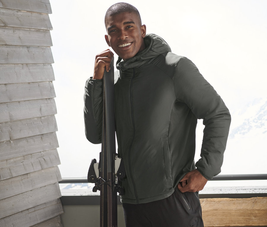 Mann in Thermo-Midlayer steht an Ski gelehnt.