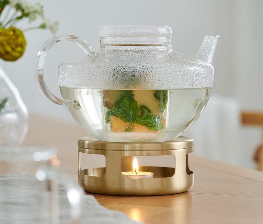 Eine klare Glas Teekanne mit Tee steht auf einem goldenen Stövchen.