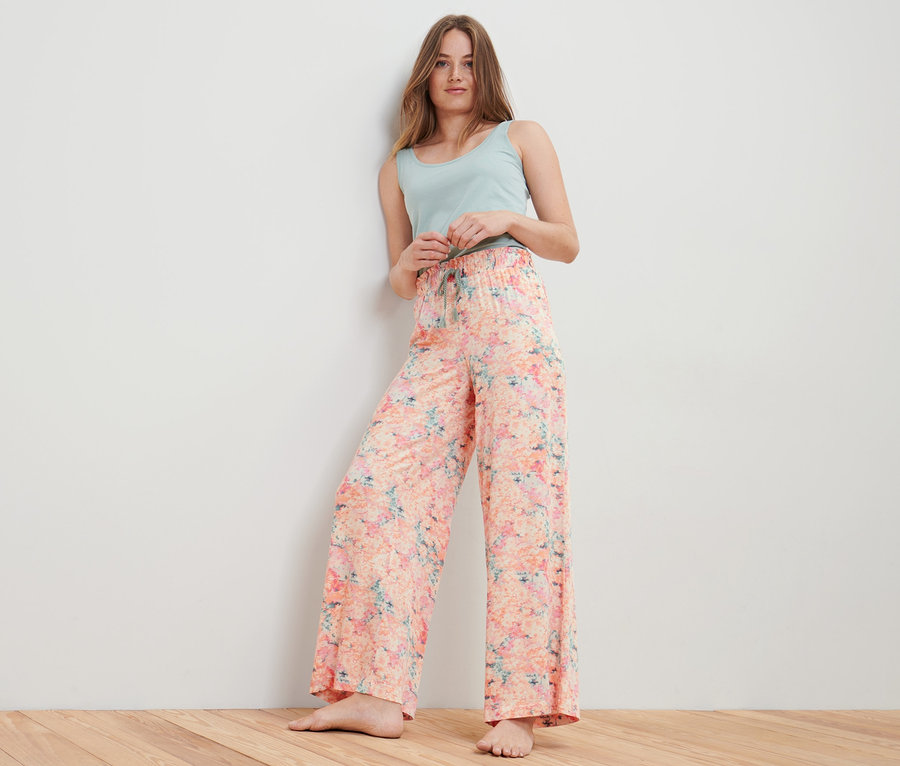 Eine Frau posiert in einer apricotfarbenen Relaxhose und einem hellblauen Top.