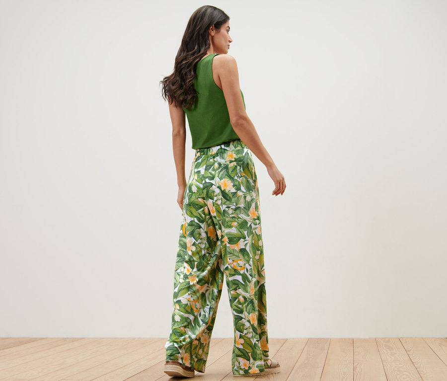 Frau posiert in grünem Top und bedruckter Palazzohose.