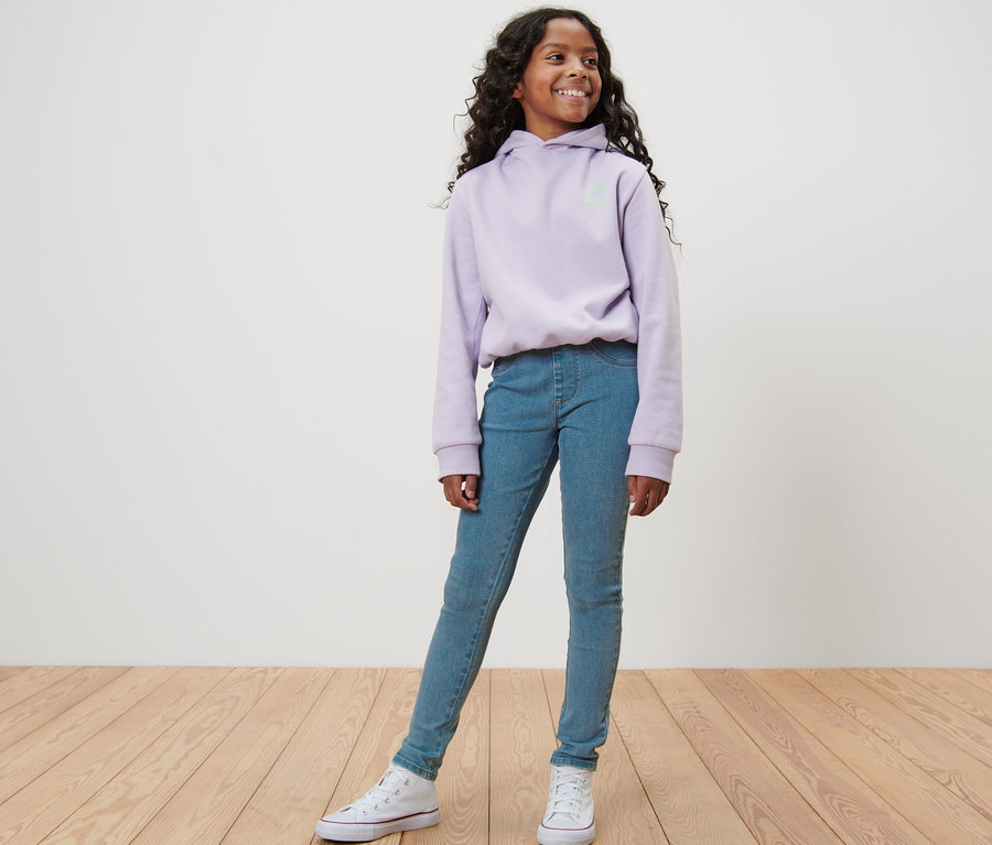 Mädchen posiert in blauen Kinder-Treggings – Fit »Jule« und lila Kapuzenpullover.
