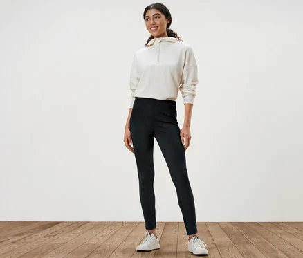 Frau steht und trägt schwere Leggings, einen weißen Pullover und weiße Turnschuhe.