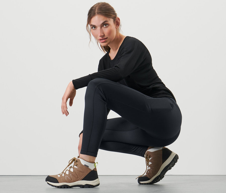 Frau hockt in schwarzer Thermotight und braunen Stiefeln.
