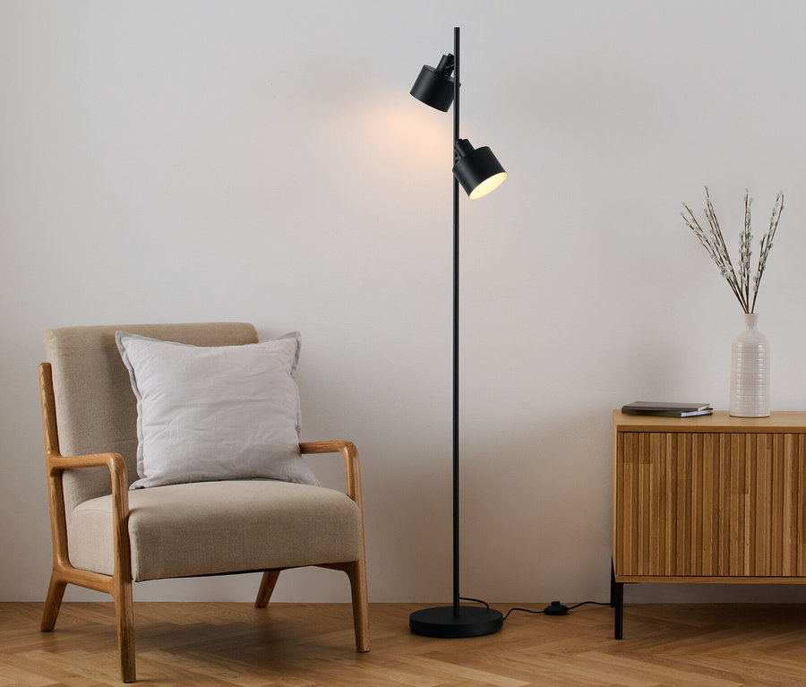 Sessel mit Kissen steht neben schwarzer Stehlampe und Holzkommode.