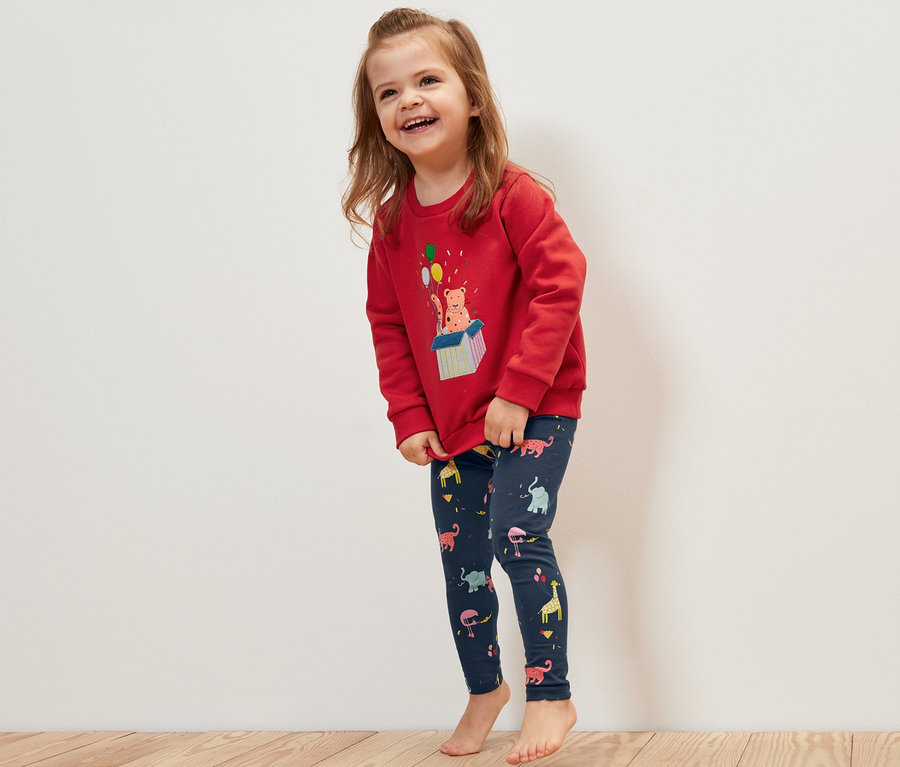 Lächelndes Mädchen trägt einen roten Pullover und 5 Kinder-Leggings mit Tiermotiven.