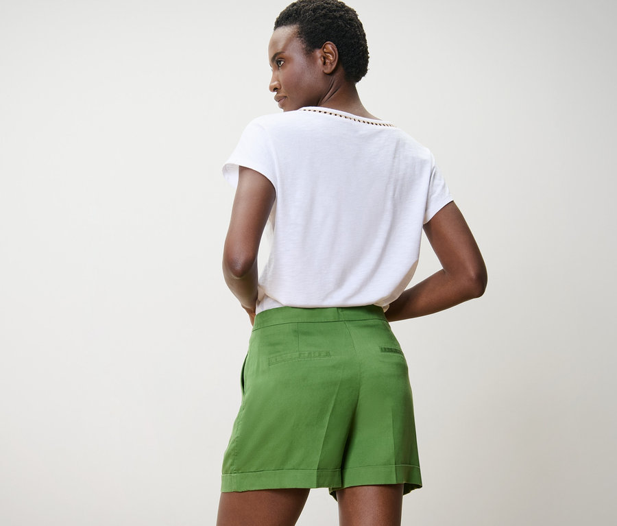 Dunkelhäutige Frau posiert von hinten in grünen Leinen-Shorts und weißem T-Shirt.