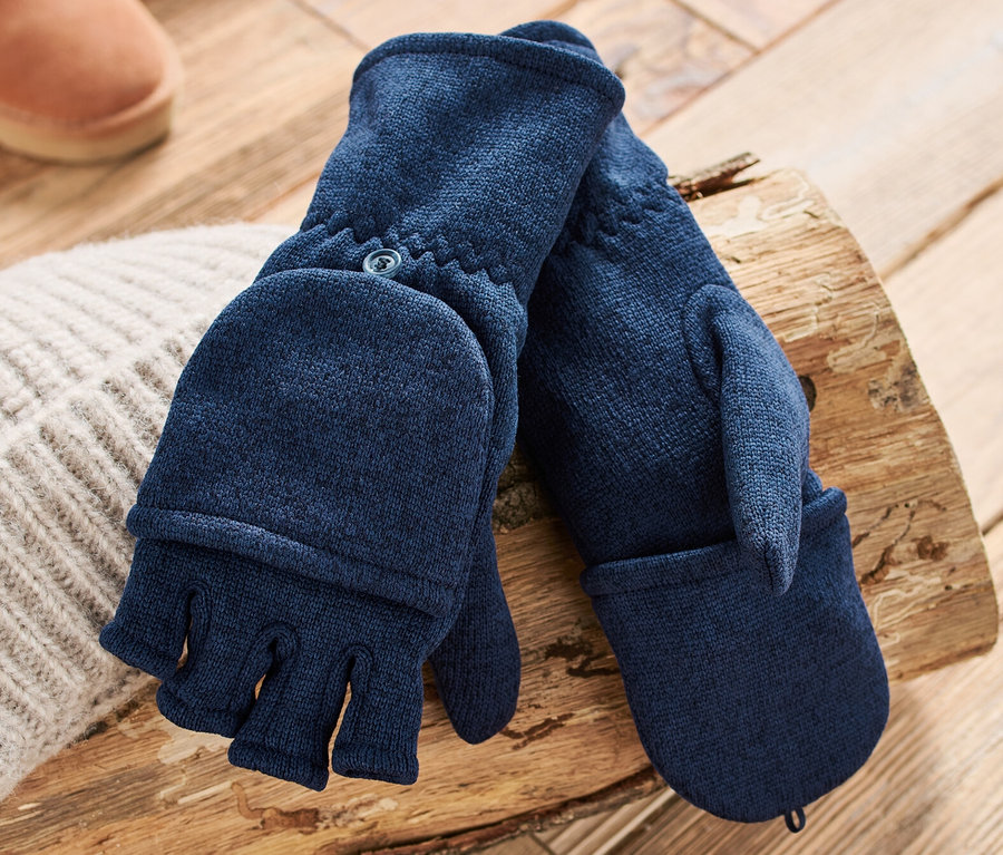 Dunkelblaue Strickfleece-Klappfäustlinge liegen auf einem Holzscheit neben einer Strickmütze und braunen Stiefeln.