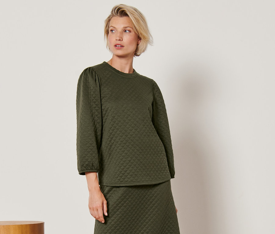 Frau posiert in grünem Shirt in Steppoptik und Rock.