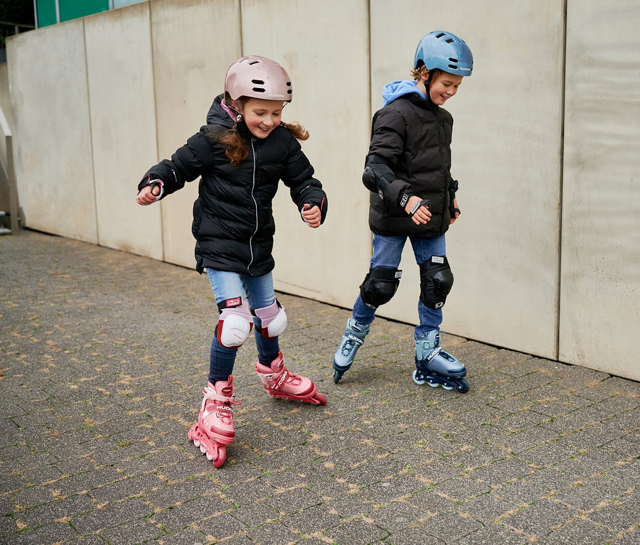 Zwei Kinder fahren mit HUDORA Inline Skates »Mia 2.0« und Schutzausrüstung.