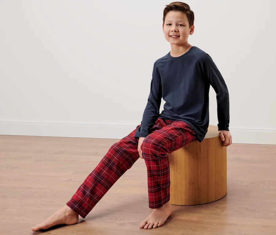 Ein Junge sitzt auf einem Hocker und trägt einen Kinder-Flanell-Pyjama.