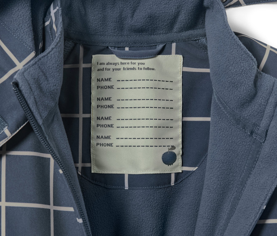 Detailansicht eines karierten Kleinkind-Softshell-Einteilers mit einem Etikett für Name und Telefonnummer.