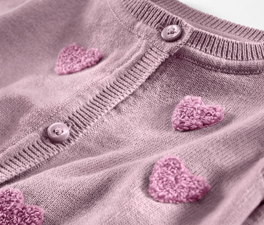 Detailaufnahme einer Kinder-Strickjacke mit aufgenähten rosa Herzen und Knöpfen.