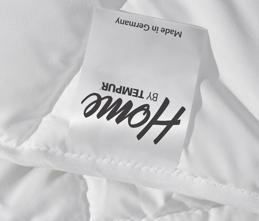 Detail einer weißen Home By TEMPUR® Luxe Duo-Decke mit gestepptem Muster und Etikett Made in Germany.