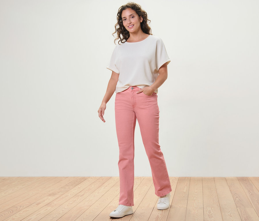 Frau posiert in korallefarbenen Bootcut Jeans ‒ Fit »Lou« und weißem Oberteil.