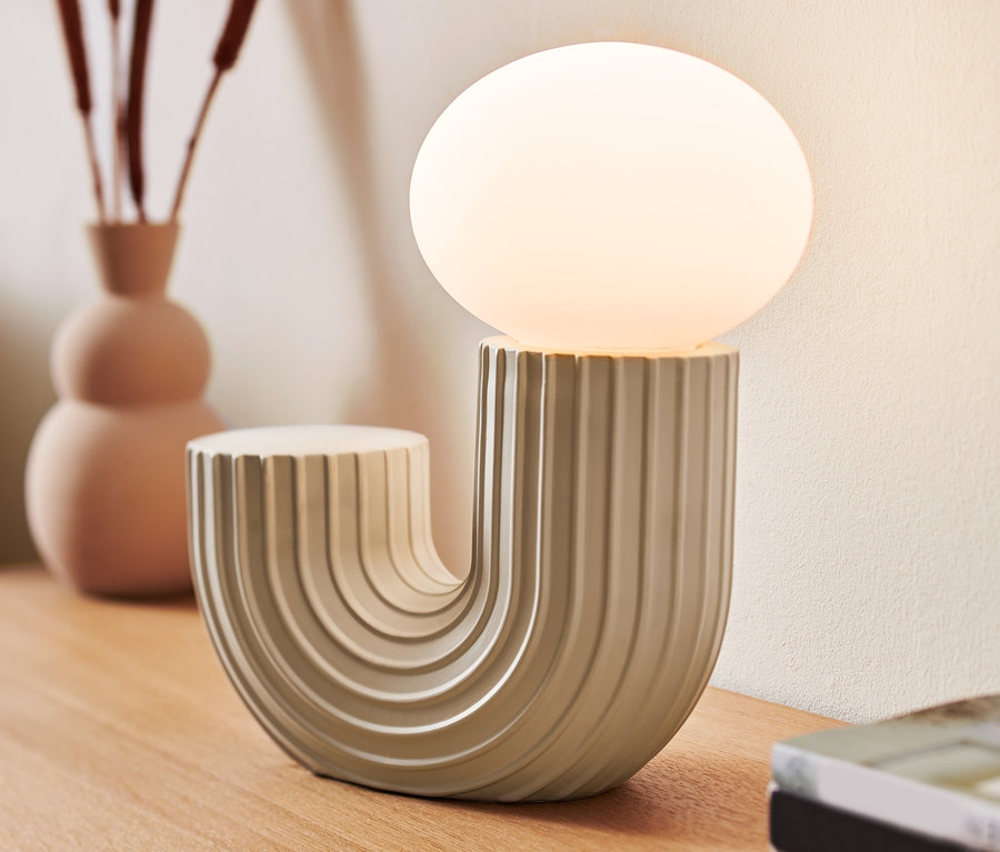 Eine LED-Design-Tischleuchte steht auf einem Holztisch neben einer Vase und Büchern.