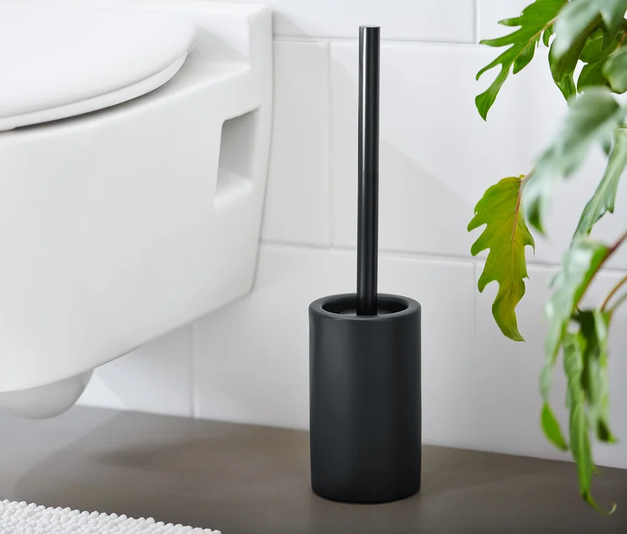 Eine schwarze WC-Bürste steht neben einer weißen Toilette.
