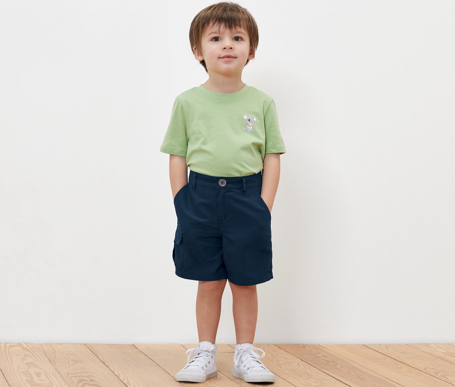 Ein Junge steht mit den Händen in den Taschen seiner Kinder-Funktionsshorts.