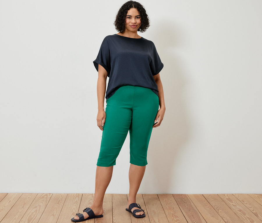 Eine Frau steht und trägt eine 3/4-Bengalin-Hose und ein Blusenshirt im Materialmix in Navy.