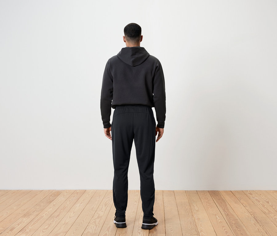 Mann von hinten trägt schwarze Hose und Hoodie.