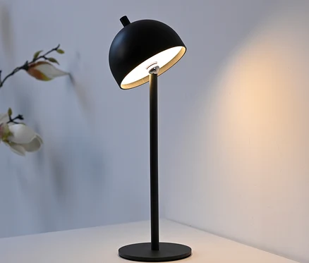 Eine schwarze Tischleuchte mit rundem Lampenschirm und Metallfuß steht auf einem weißen Tisch.